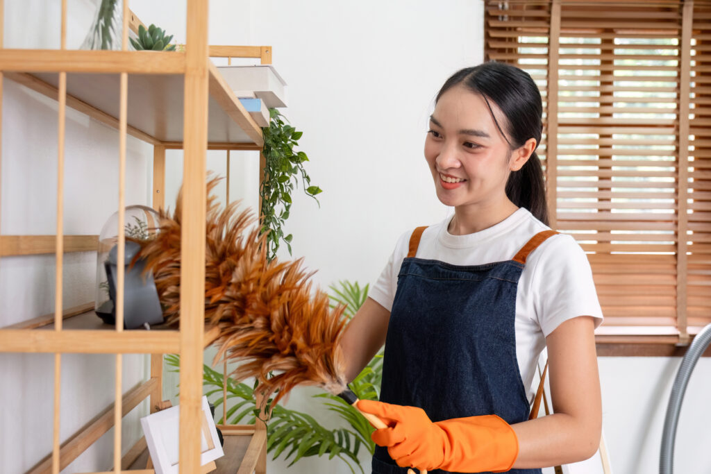 Young woman cleaning furniture in living room with house duster.